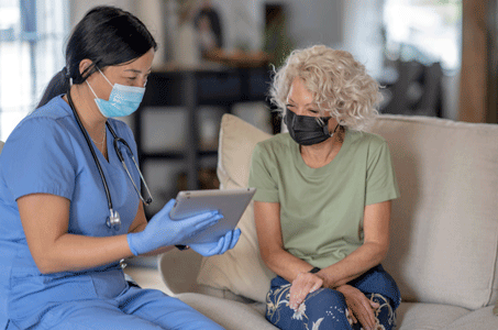 A doctor is sitting on a couch showing an older woman information on an ipad.