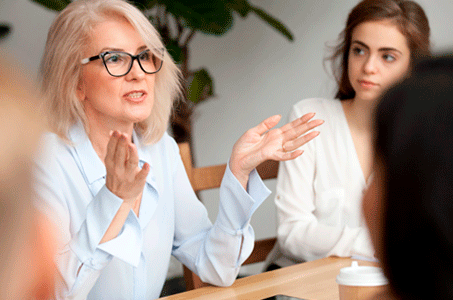A professional looking woman is explaining something to people gathered around a table.